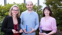 Three award winners standing in front of an outdoor landscape.